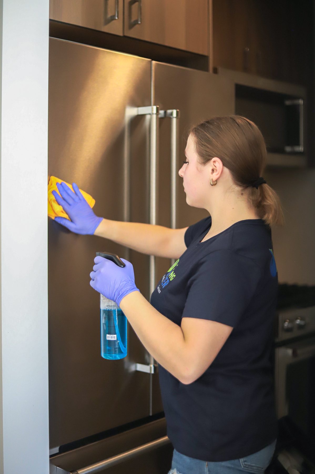 Cleaning Master professional deep cleaning a stainless steel refrigerator in an apartment kitchen