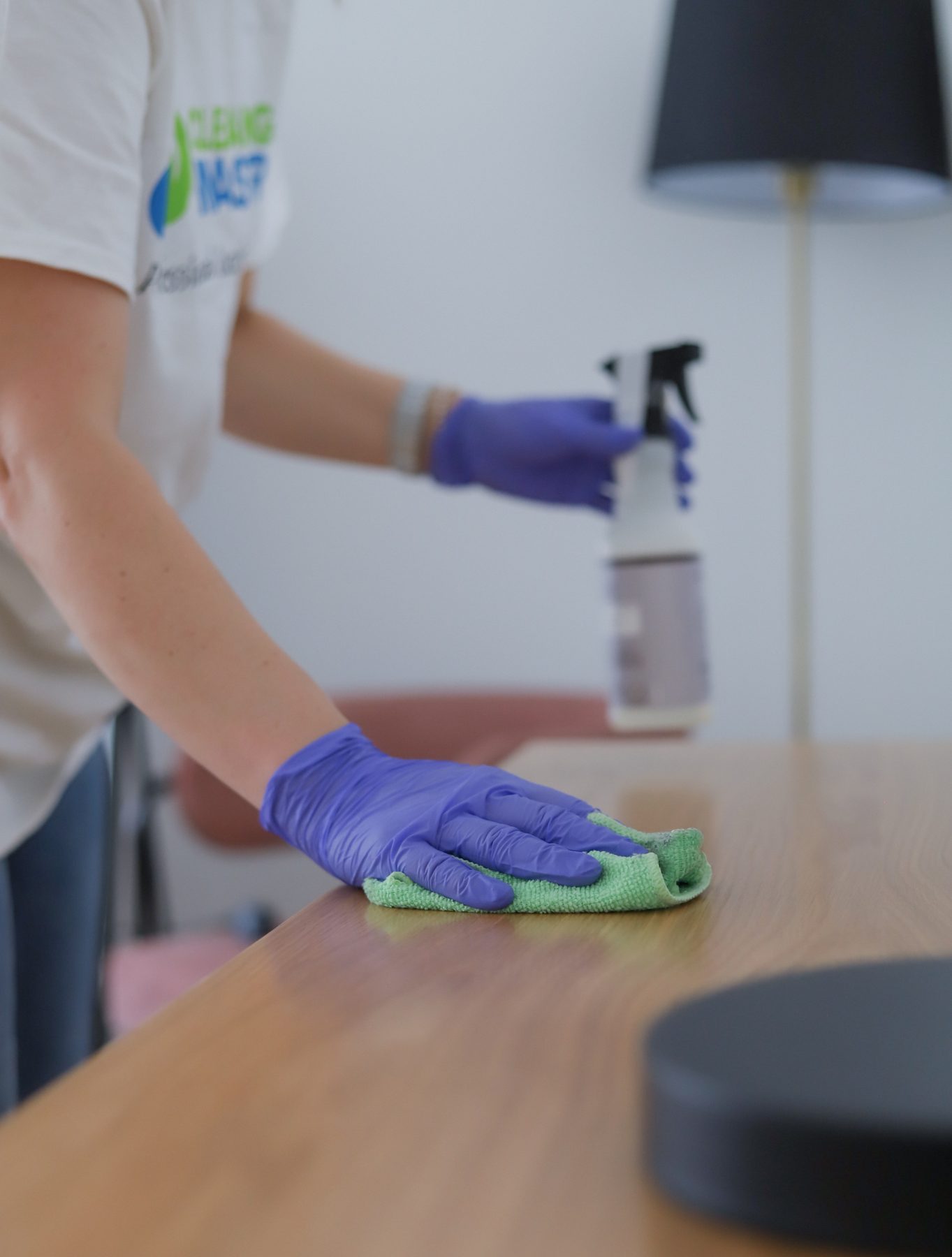 Cleaning Master professional wiping down an office desk surface with microfiber and spray