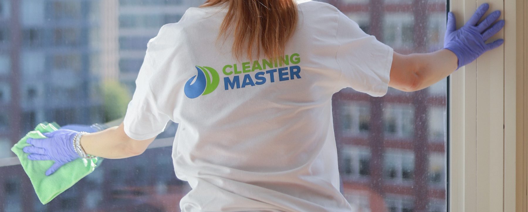 Cleaning Master professional in a branded team t-shirt cleaning a high-rise window