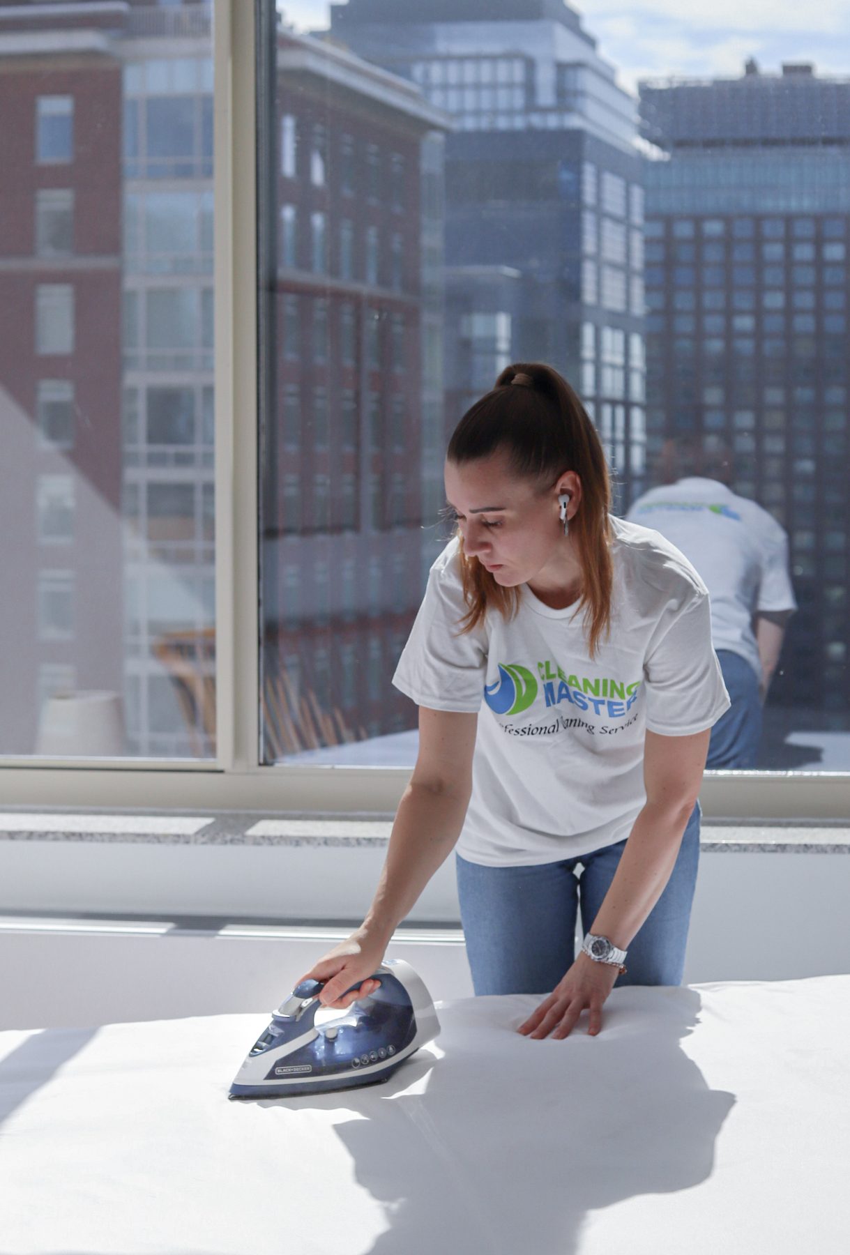Two Cleaning Master professionals working together in a Manhattan apartment, one pressing linens by the window