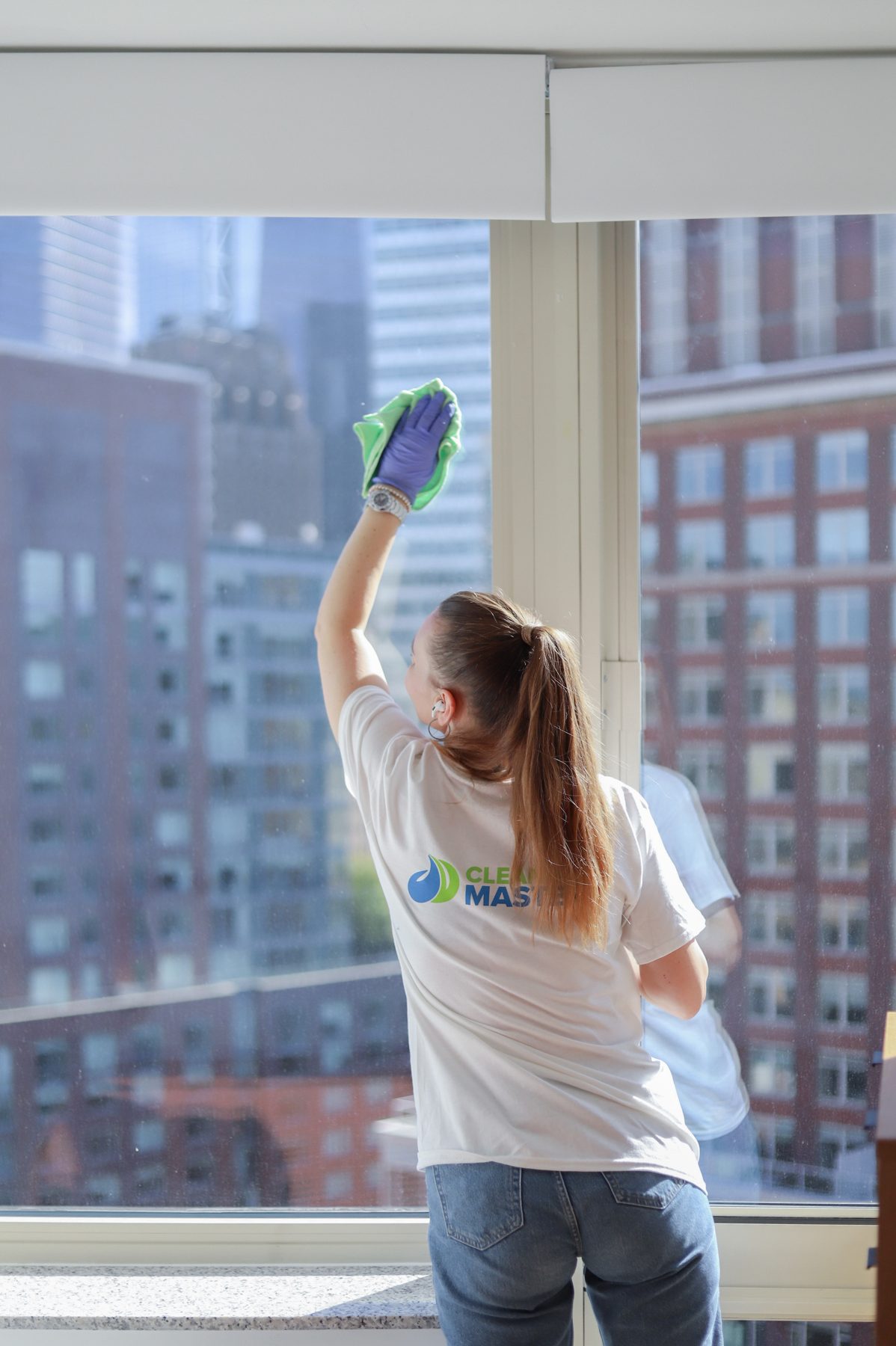 Cleaning Master professional washing post-renovation dust from a window overlooking the NYC skyline